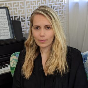 Headshot of Maya Ackerman sitting in front of a piano