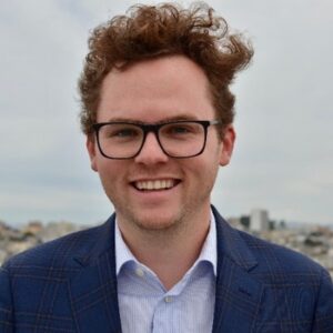 Headshot of a smiling man in spectacles wearing blue suit